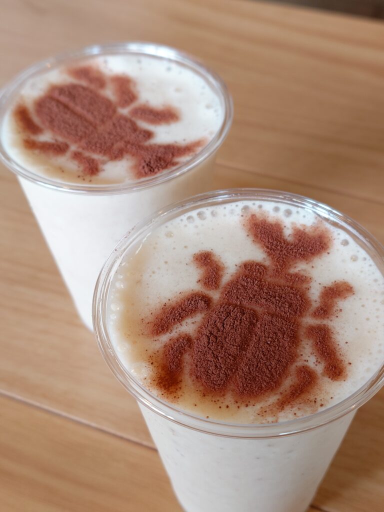 Two frothy drinks in clear cups with cocoa powder sprinkled on top, resting on a wooden table.