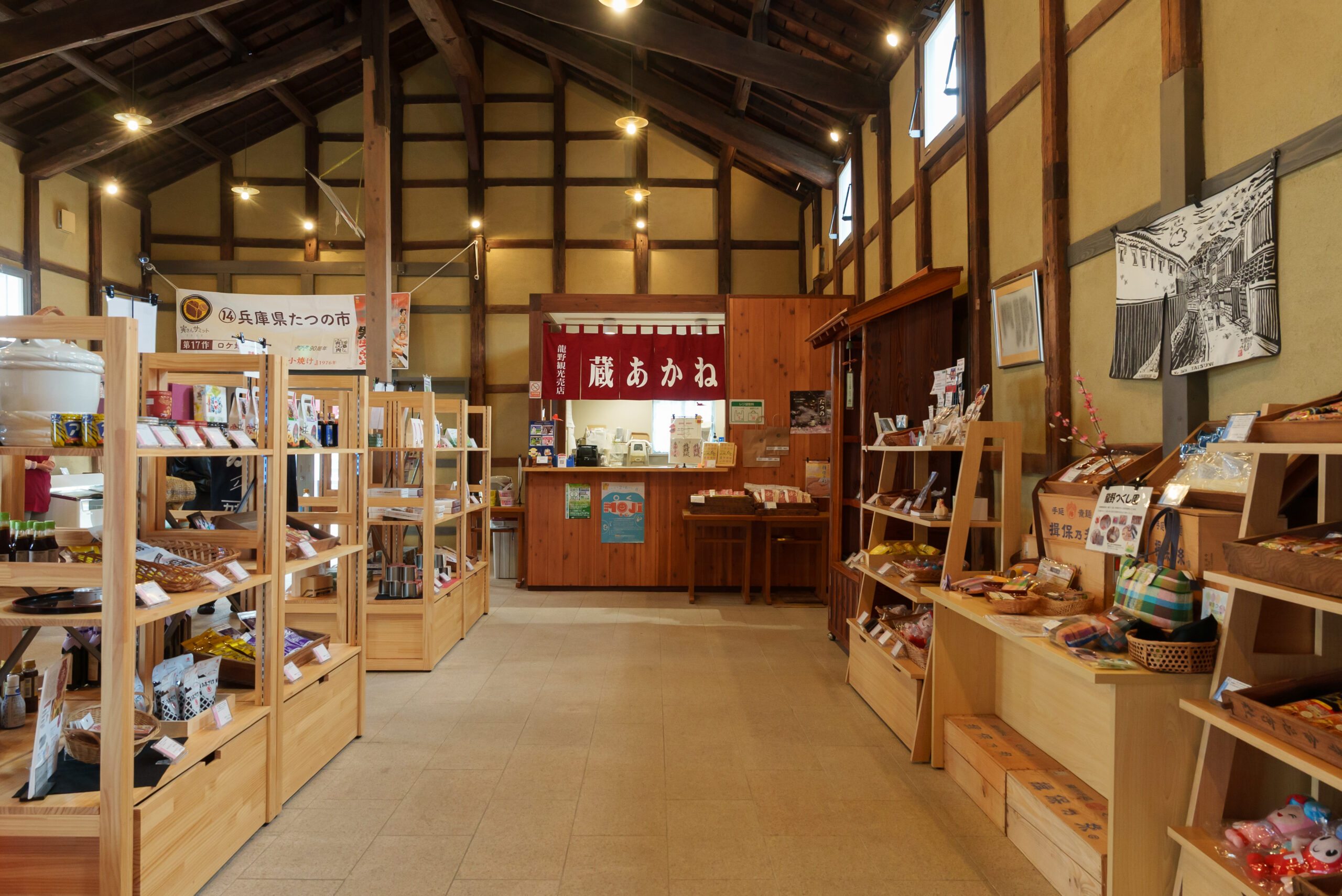 Interior of a rustic Japanese souvenir shop with wooden shelves and beams, shelves stocked with snacks and gifts, warm lighting, and banners displayed in the back.