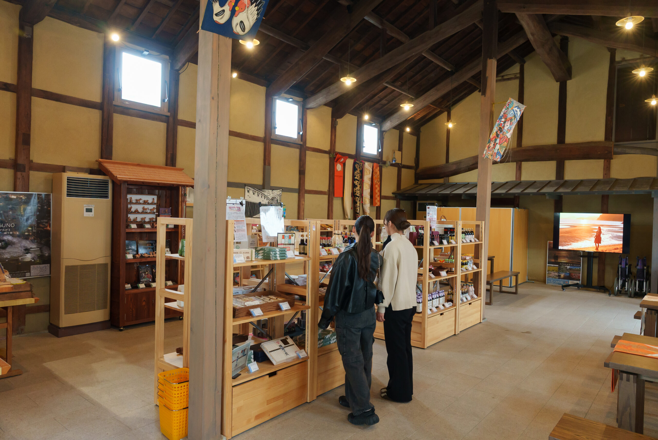 Interior of a souvenir shop with exposed wooden beams, tall shelves of books and trinkets, and two women browsing displays.