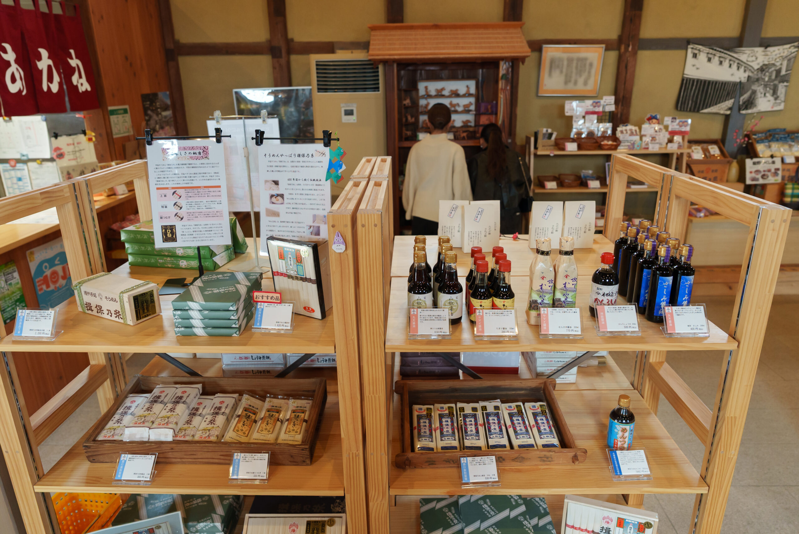 Interior of a Japanese shop with wooden display shelves filled with bottled sauces and packaged goods on tables and shelves.